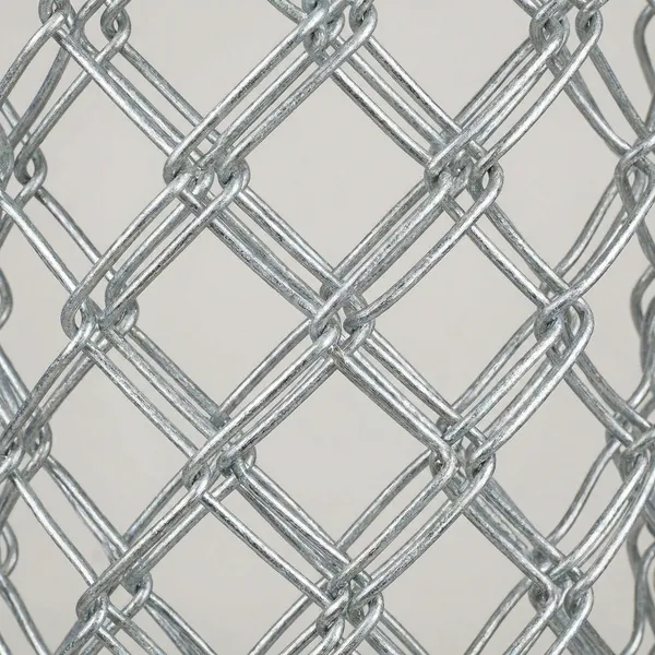 Close-up detail of galvanized chain link fence material showing the diamond pattern mesh and twisted wire structure against a light background.