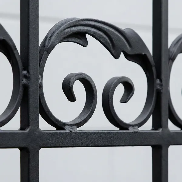 Close-up detail of black ornamental iron fence featuring elegant spiral scrollwork against a light background. Textured metal curls create a decorative pattern typical of premium wrought iron fencing.